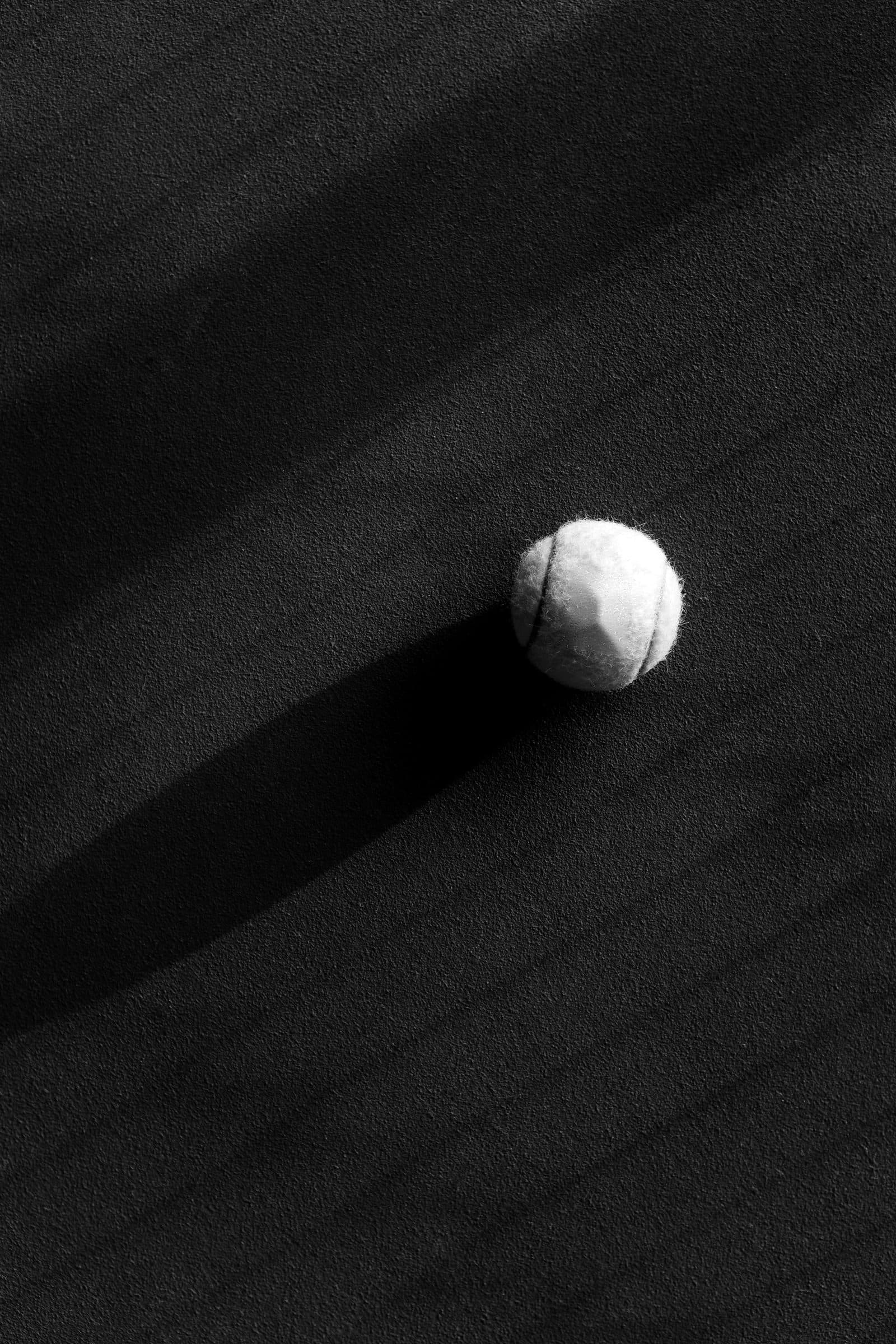 Padelball mit langem Schatten auf dunklem Court